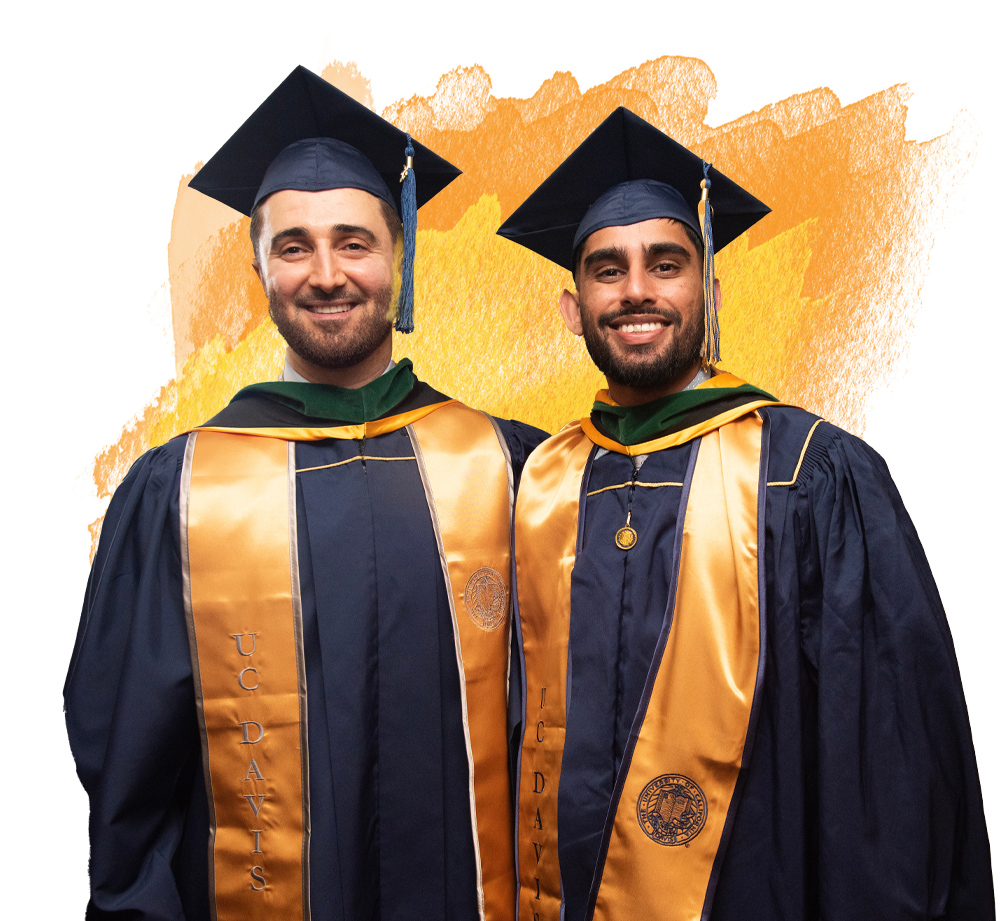 Two graduates in navy blue caps and gowns with gold UC Davis stoles smile stand side by side. An orange watercolor background appears behind them.